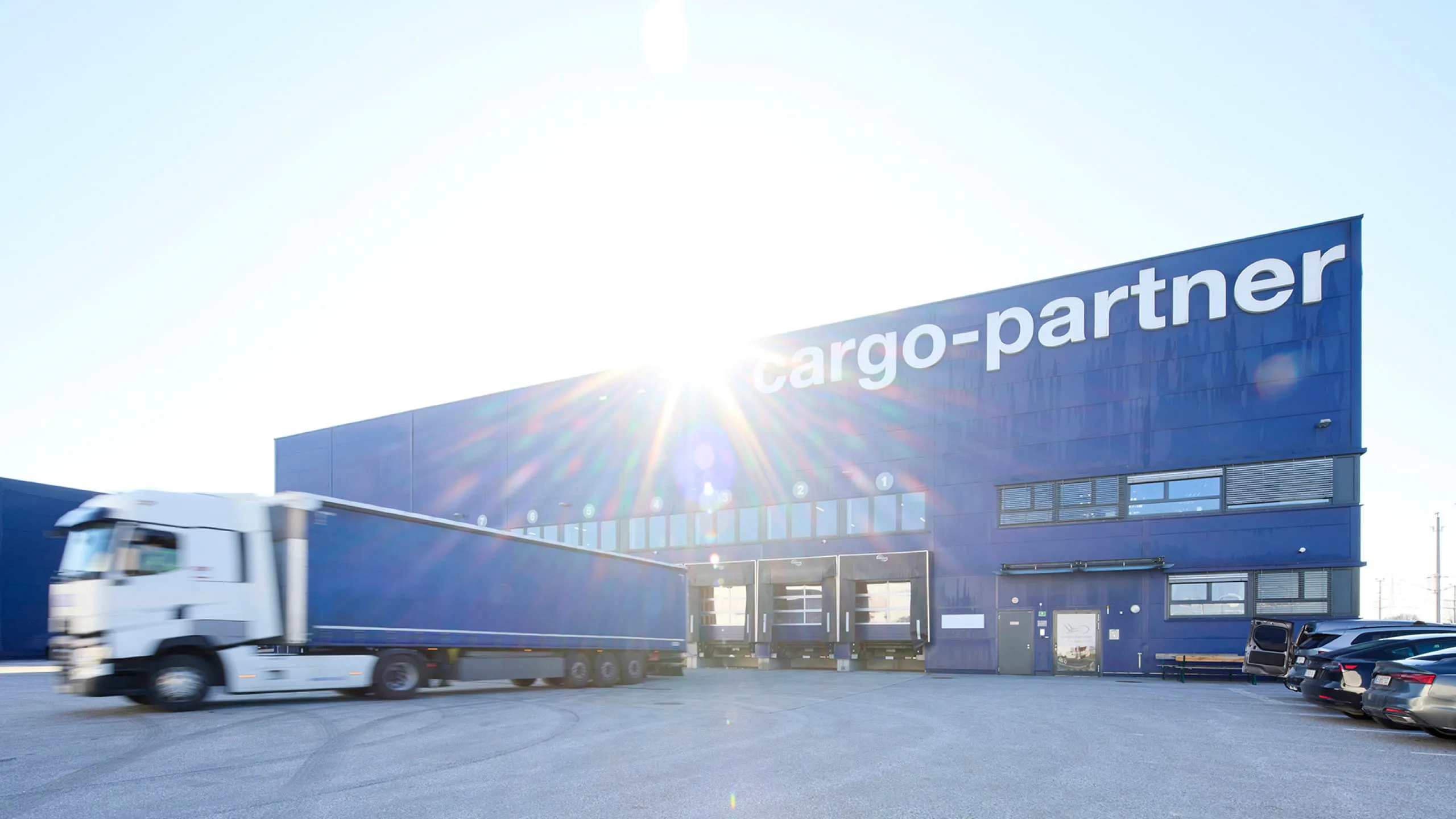 Logistikgebäude von cargo-partner mit Pletzer Immobilien, blauer Hallenbau und anliefernder LKW.